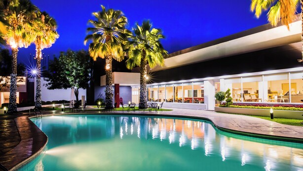 A swimming pool with palm trees and a building with large windows in the background.
