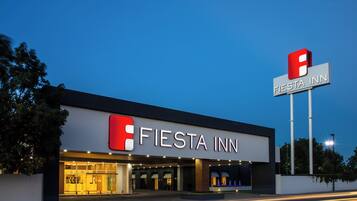 A modern hotel with a prominent 'Fiesta Inn' sign, featuring a red and white logo.