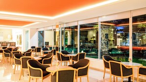 A modern indoor dining area with glass walls, wooden chairs, and tables.