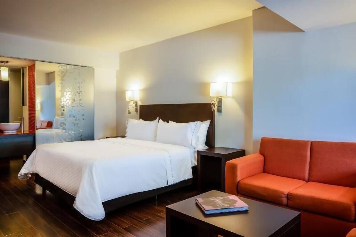 Ein Hotelzimmer mit Bett, Nachttisch, rotem Sofa und Spiegel.