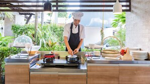 Un chef preparando comida en una cocina con vistas al exterior, donde se ve vegetación.