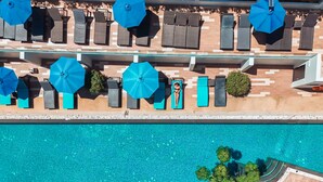 Vista aérea de un área de piscina con sillones de descanso y sombrillas.