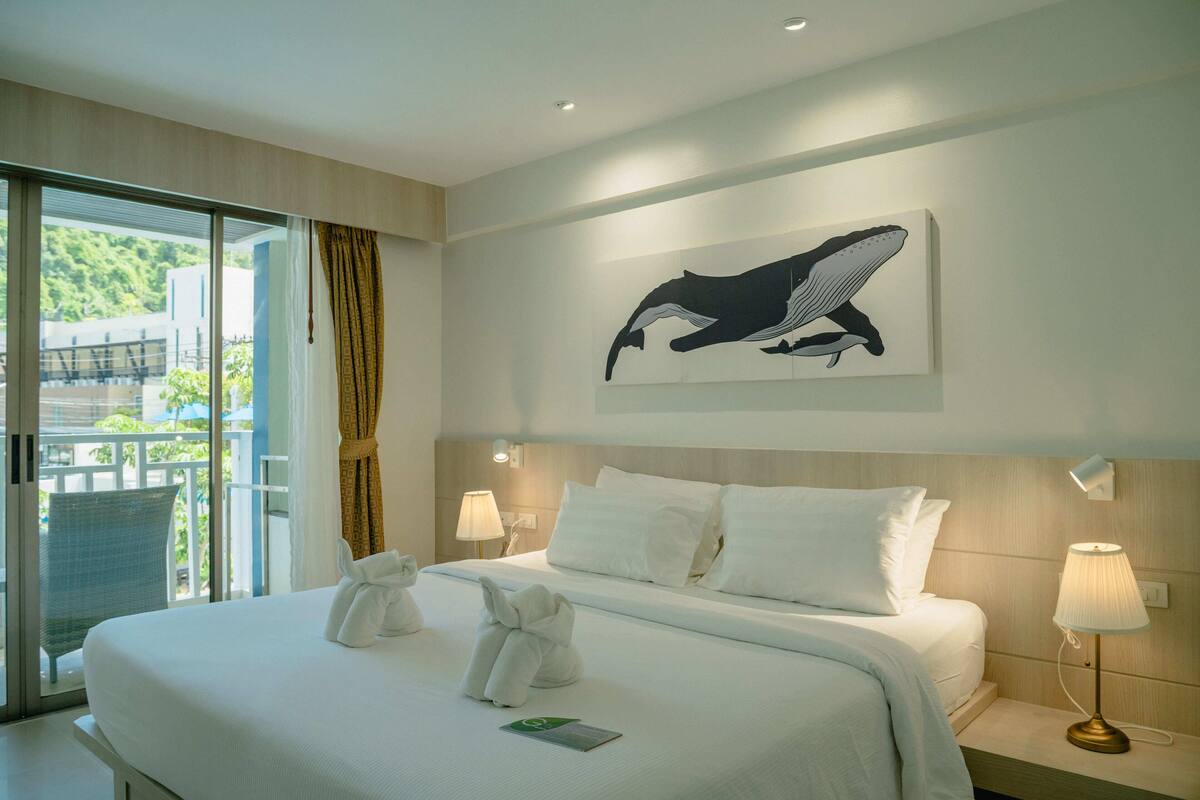 Habitación de hotel con una cama grande, vistas al exterior, un cuadro de una ballena y una lámpara en la mesita de noche.