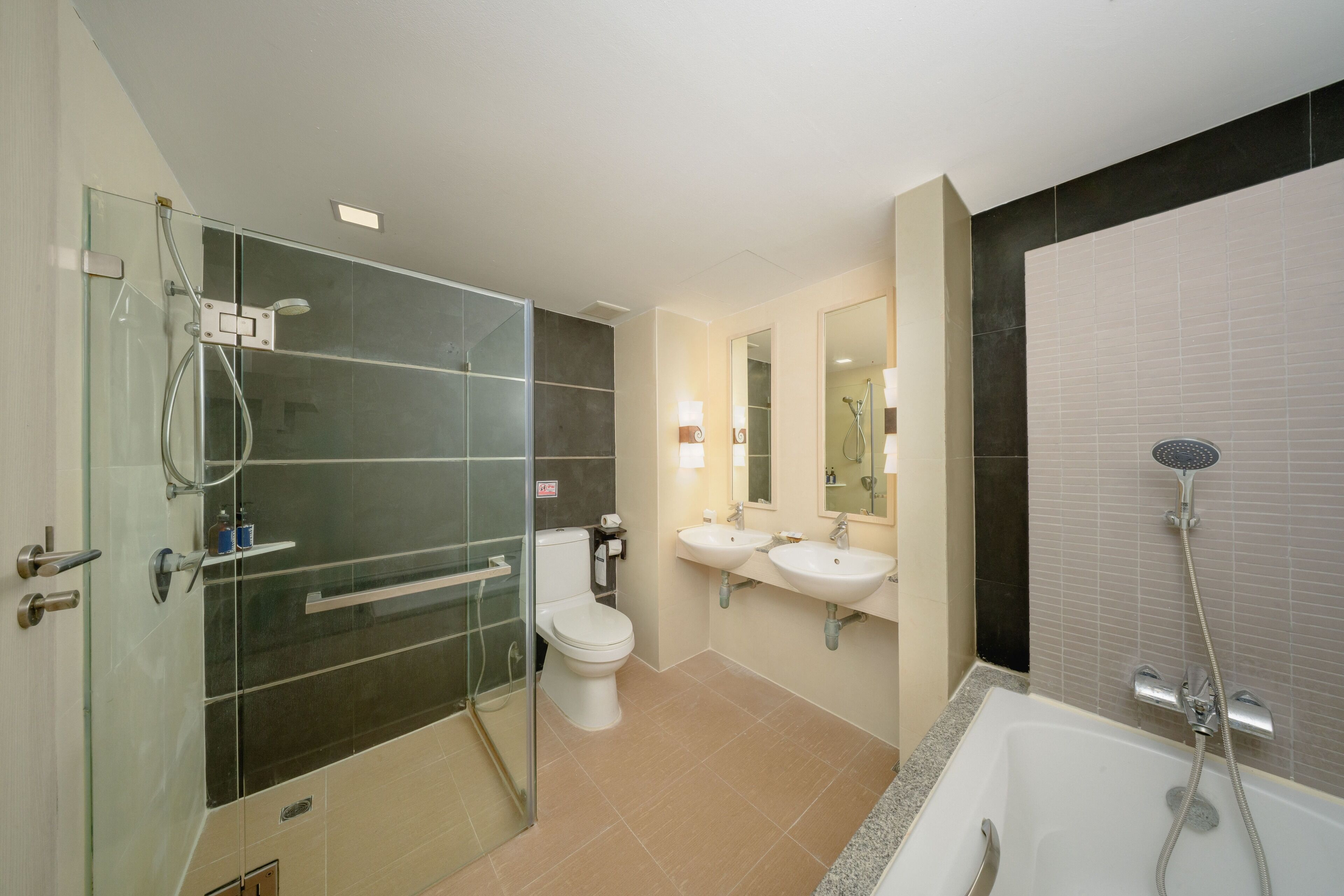 Un baño moderno con ducha de vidrio, inodoro blanco, dos lavamanos y una bañera.