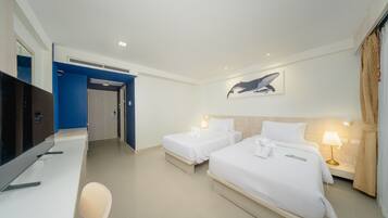 A hotel room with two beds, a desk, a TV, and a painting of a whale on the wall.