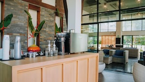 Un moderno mostrador de recepción con una máquina de café, tazas apiladas y una zona de estar con sofás y una mesa de centro.