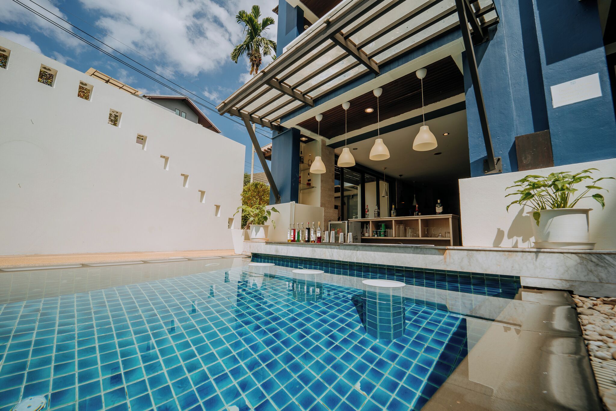A modern pool area with a tiled floor, a bar area with shelves of bottles, and a covered seating area.