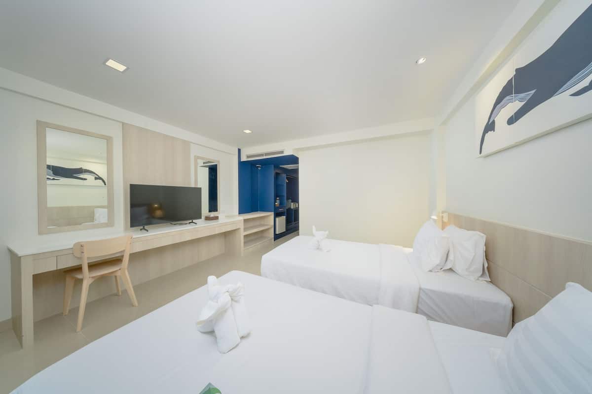 Habitación de hotel con dos camas, un escritorio, una silla y una televisión.