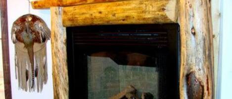 Una chimenea de madera rústica con detalles de piedra, un tapiz decorativo y un jarrón en el suelo.