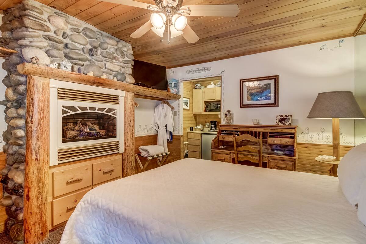A cozy bedroom with a stone fireplace, wooden furniture, and a bed.