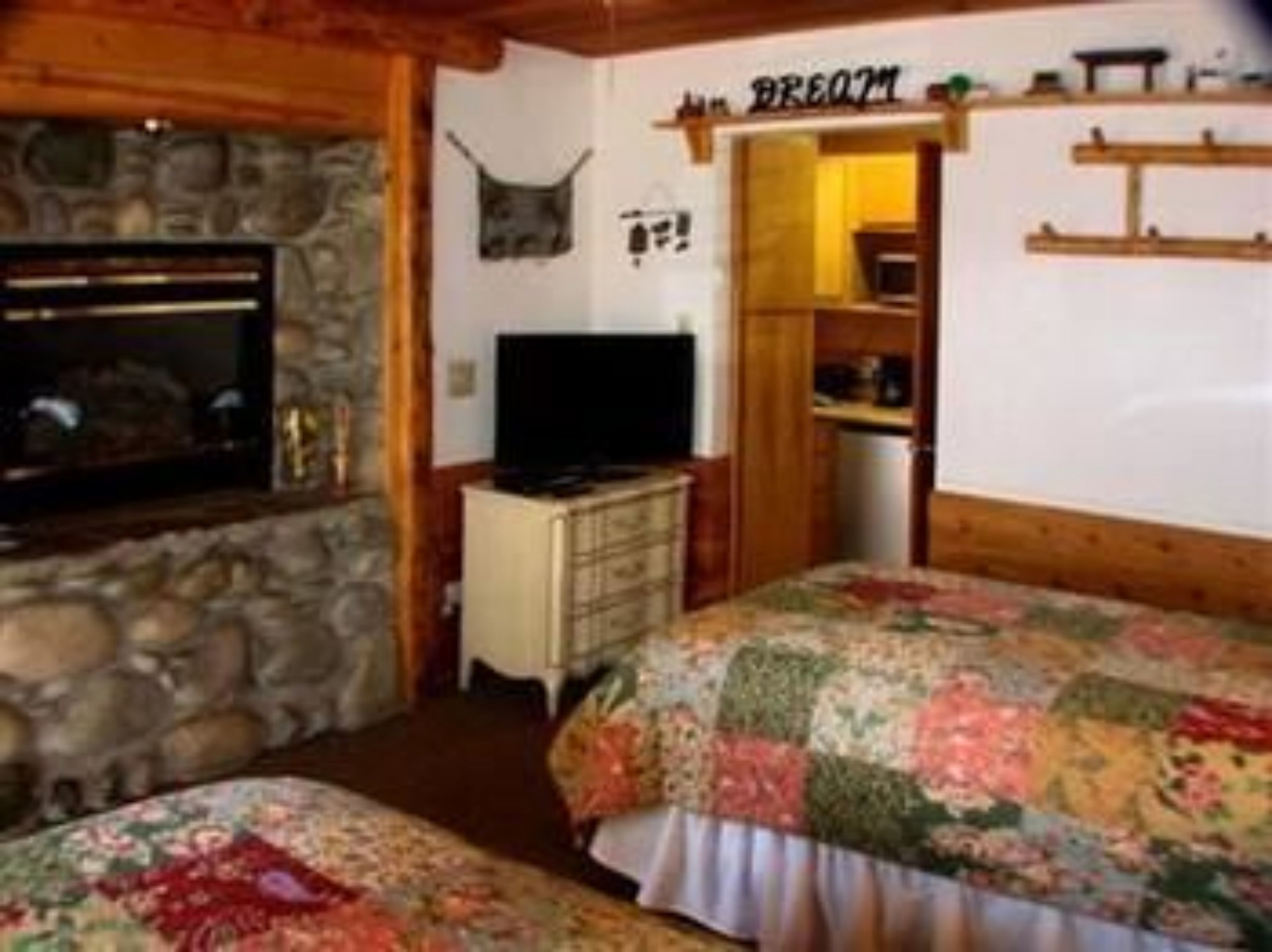 A cozy room with a stone wall, a television, a bed with floral bedding, and a sign that reads "BREOM".