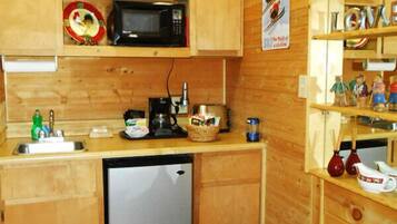 A compact kitchen with wooden cabinets, a microwave, a coffee maker, and a small refrigerator.