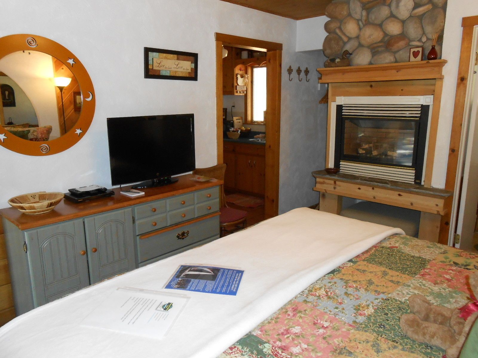 A bedroom with a television, dresser, and a fireplace.