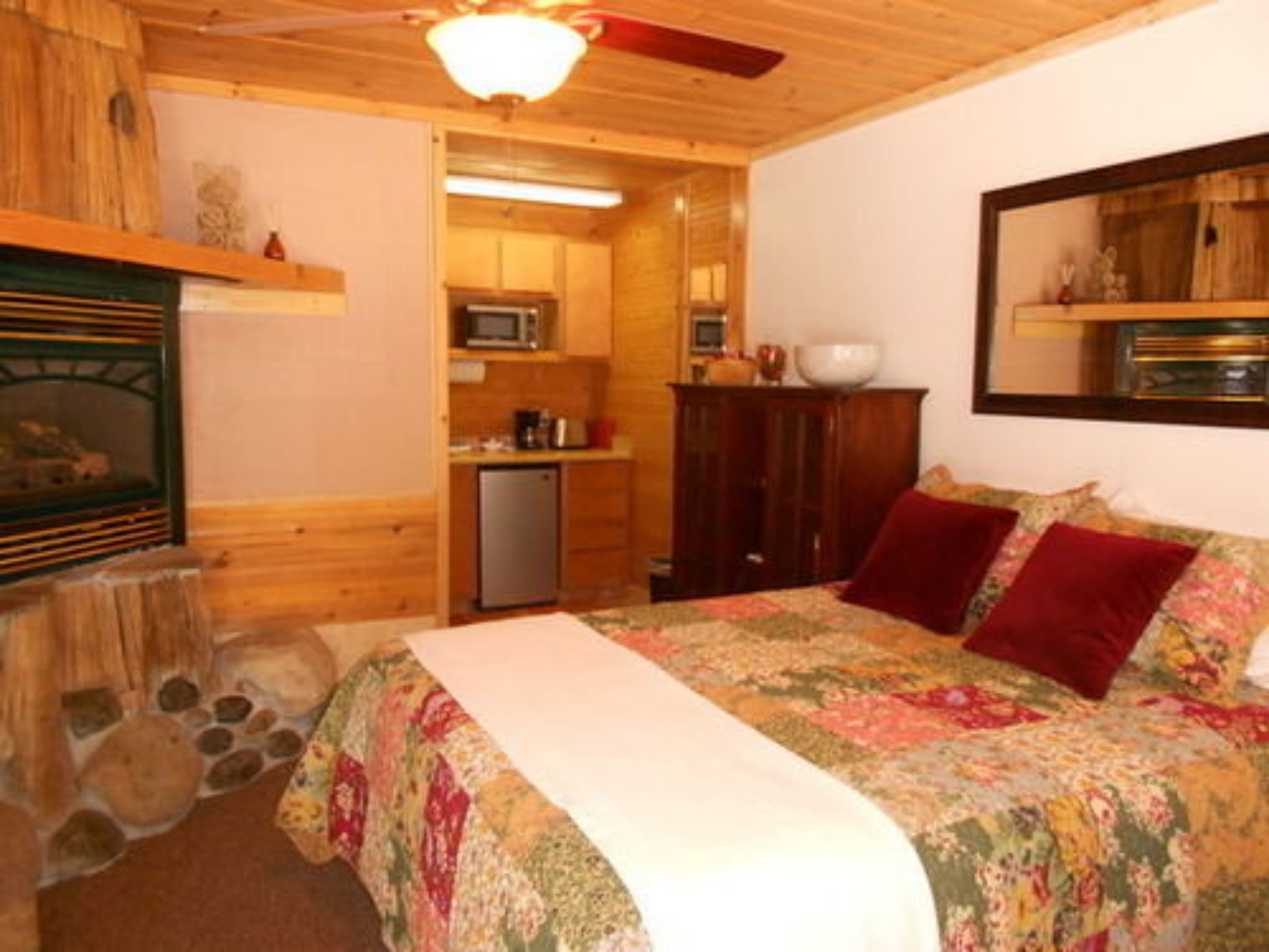 Una habitación acogedora con cama, chimenea, una pequeña cocina y un espejo en la pared.