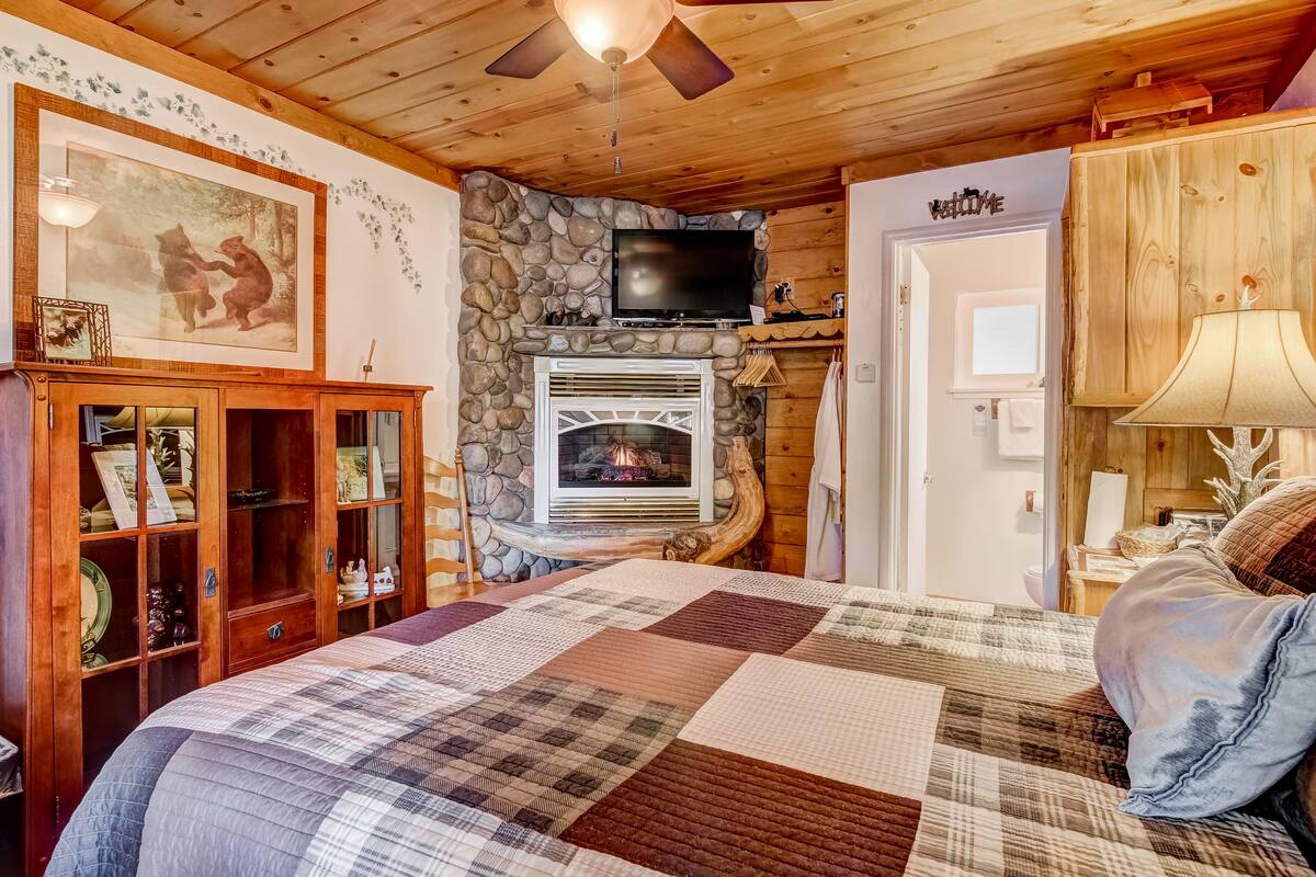 A cozy room with a fireplace, wooden ceiling, and a bed with a quilt.