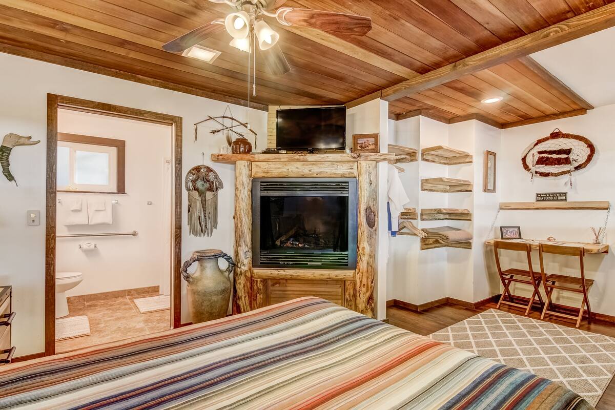 A rustic room with a fireplace, wooden ceiling, and a bed with striped bedding.