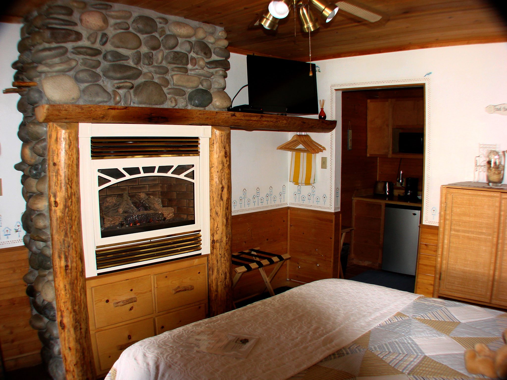 Una habitación rústica con pared de piedra, muebles de madera, chimenea y televisor.