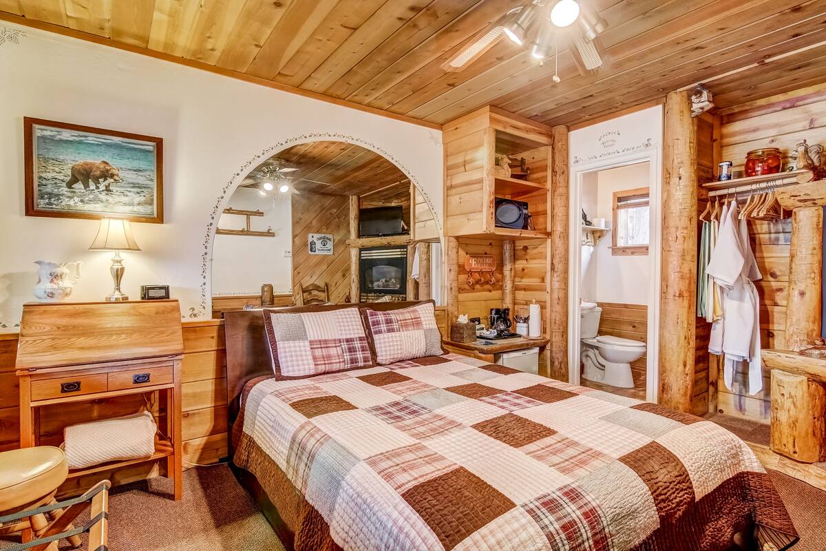 A cozy wooden cabin bedroom with a large bed, a desk, and a built-in fireplace.
