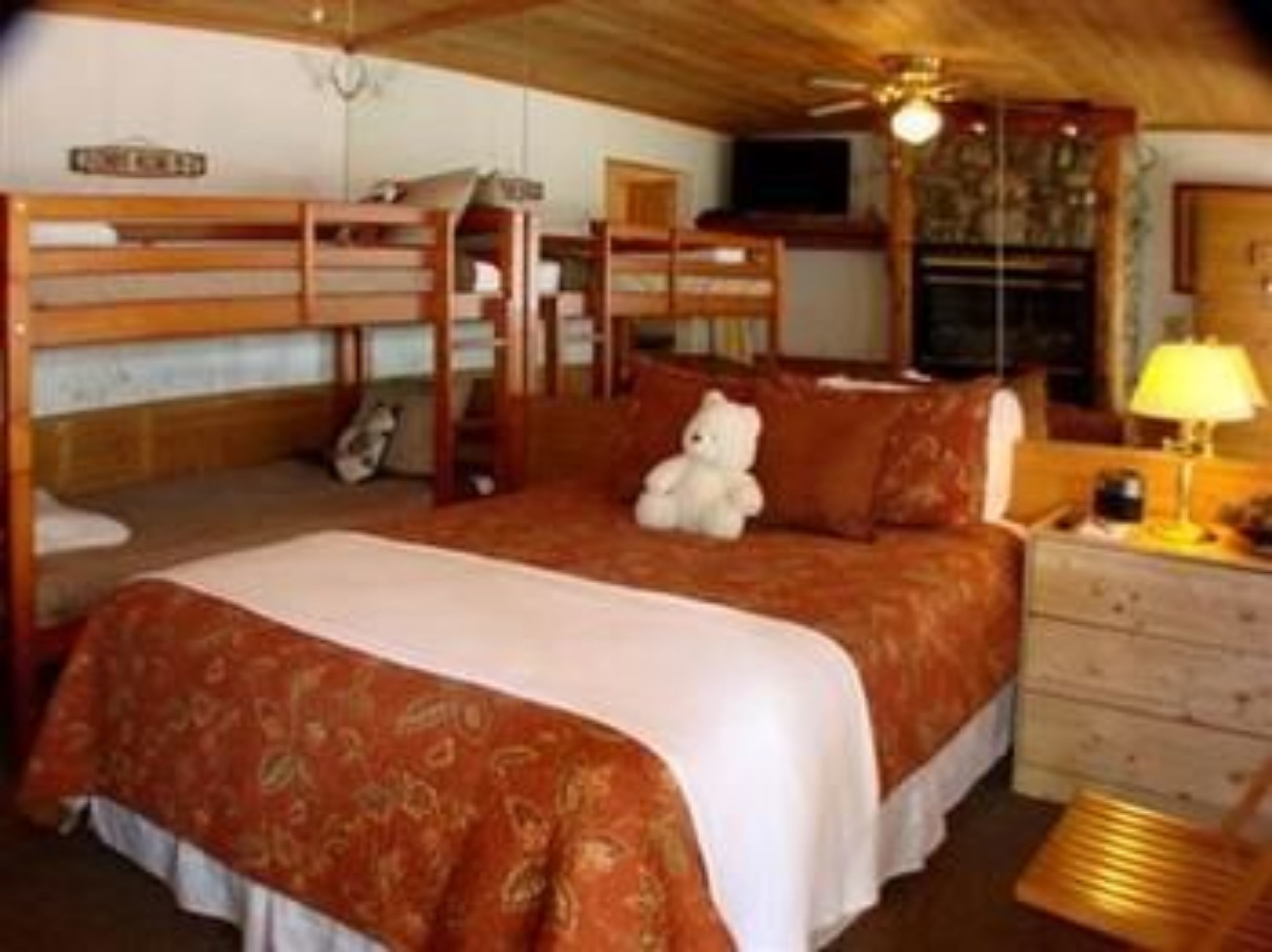A bunk bed room with a wooden ceiling, a television, and a teddy bear on the bed.