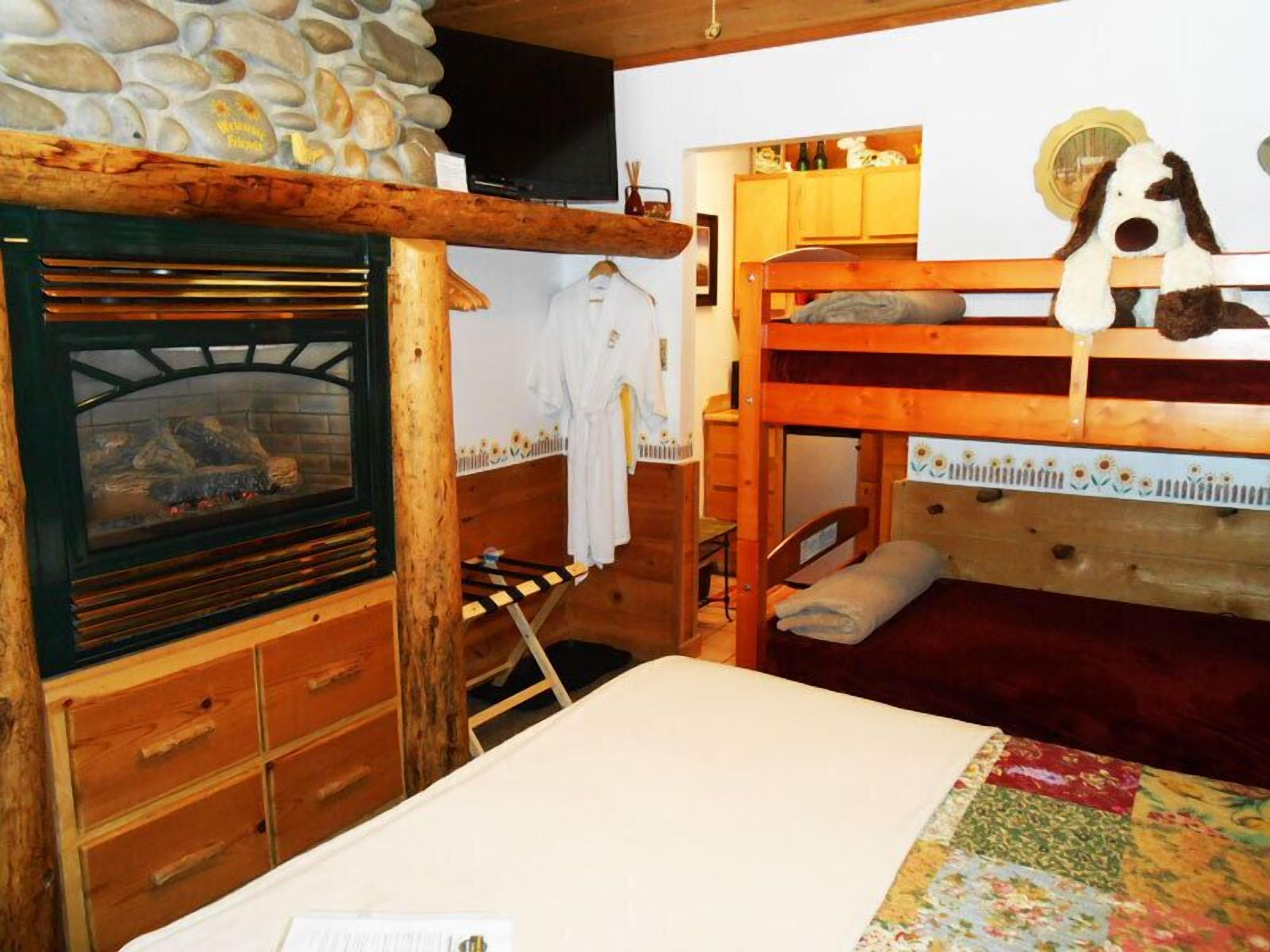 Una habitación rústica con pared de piedra, literas de madera, chimenea y colcha acolchada.