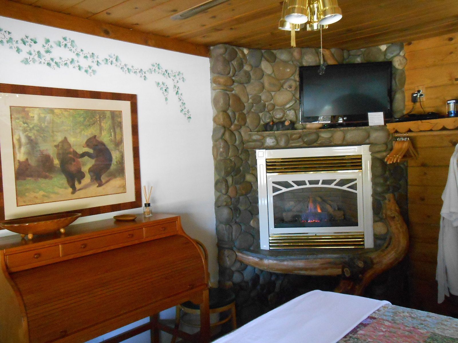 A cozy room with a stone fireplace, a television mounted above it, and a painting of bears on the wall.