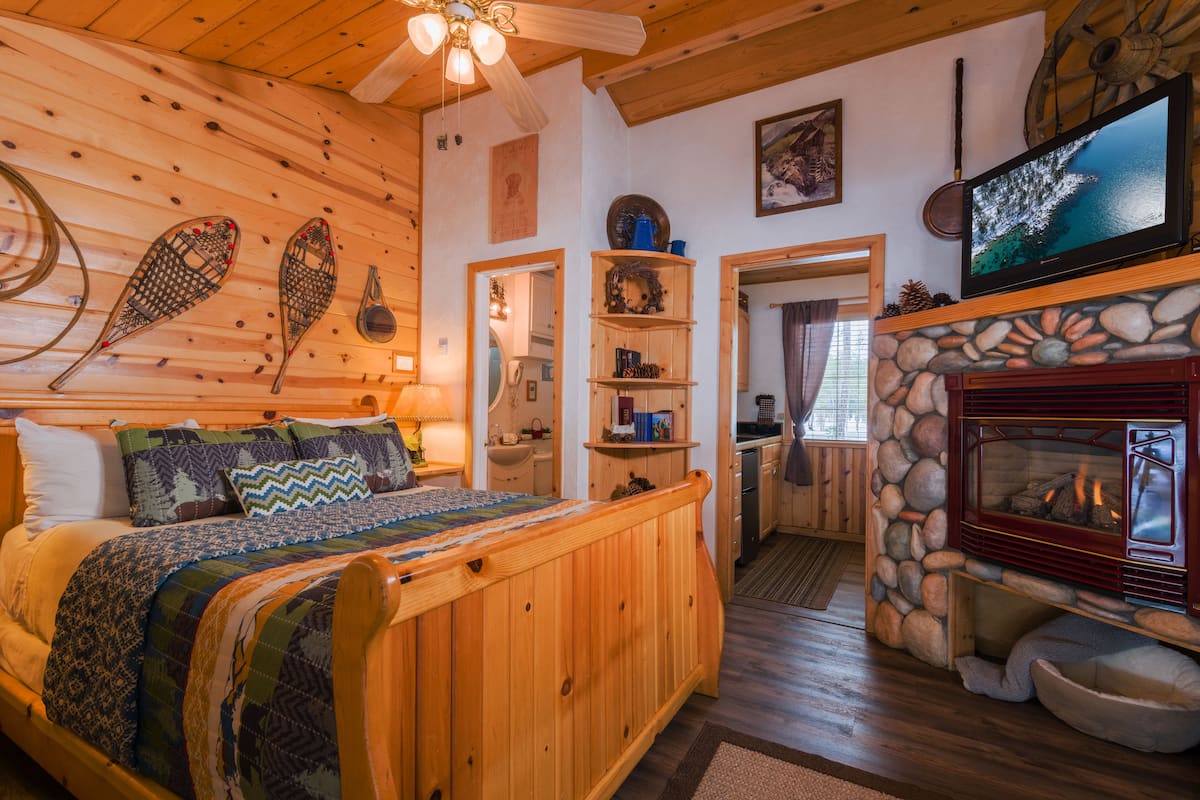 A cozy cabin interior with a wooden bed, a stone fireplace, and a television mounted above it.
