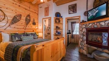 Ein gemütliches Blockhauss-Interieur mit einem Holzbett, einem Kamin aus Stein und einem darüber montierten Fernseher.