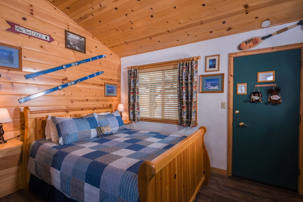 A cozy room with a wooden bed, a window with blinds, and a door with a sign.