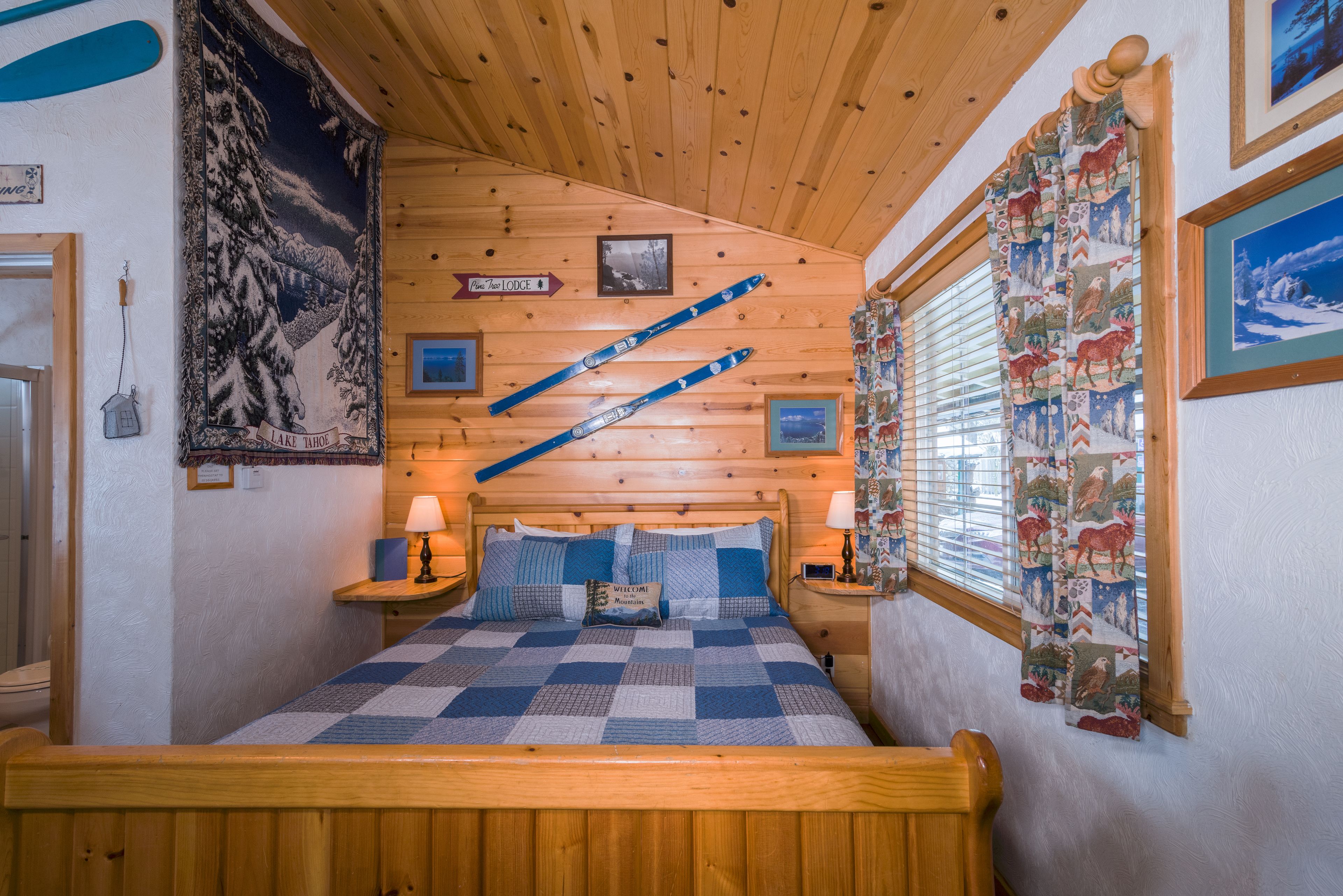 A cozy room with a wooden bed, a checkered quilt, and a mountain-themed tapestry.