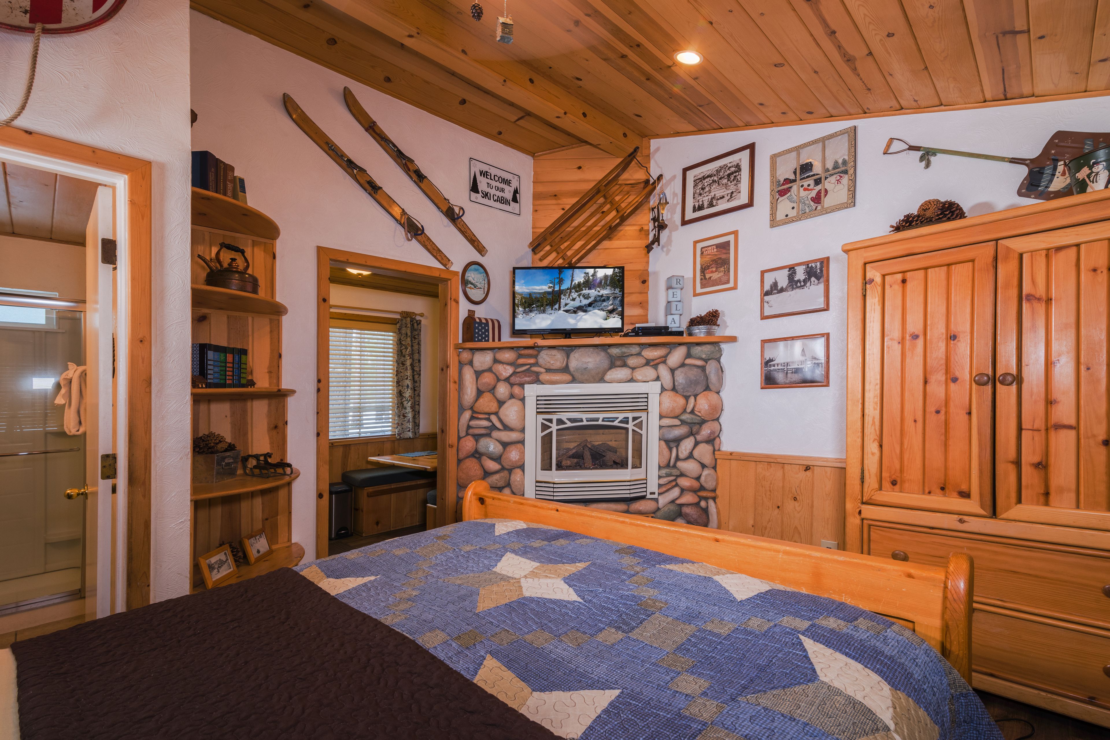 Une pièce chaleureuse avec une cheminée en pierre, des étagères en bois, un lit recouvert d’une courtepointe et, accroché au mur, du matériel de ski.