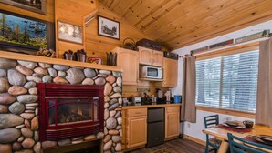 A cozy cabin interior with a stone fireplace, wooden cabinets, a kitchen area, and a dining table with chairs. - Fireside Lodge (South Lake Tahoe)