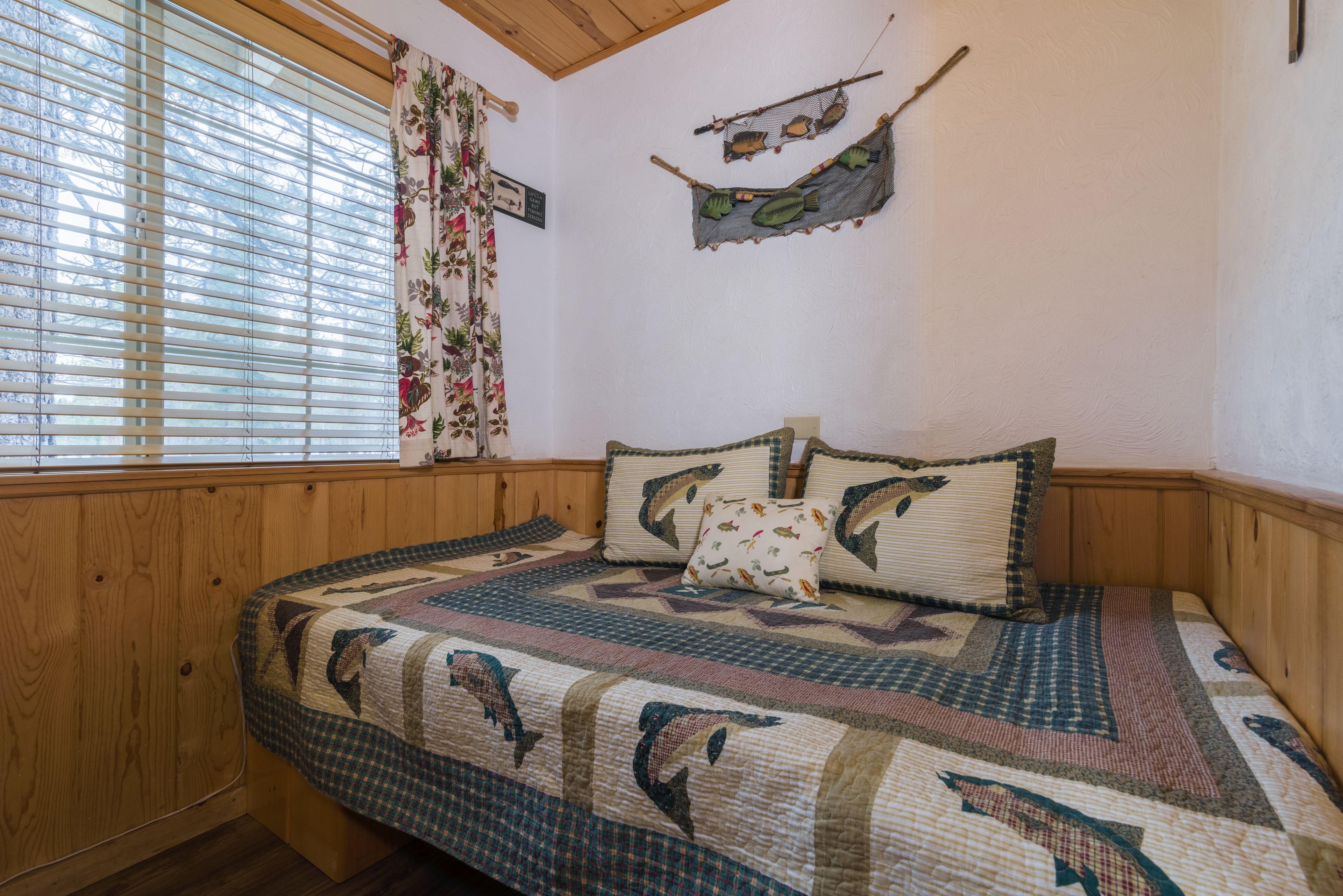 Una camera da letto con un letto a castello in legno, una coperta con motivi di pesci, un'amaca appesa al muro e una finestra con persiane.