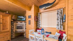 A wooden cabin interior with a stone fireplace, wooden dining table, white chairs, and a large window with curtains. - Fireside Lodge (South Lake Tahoe)
