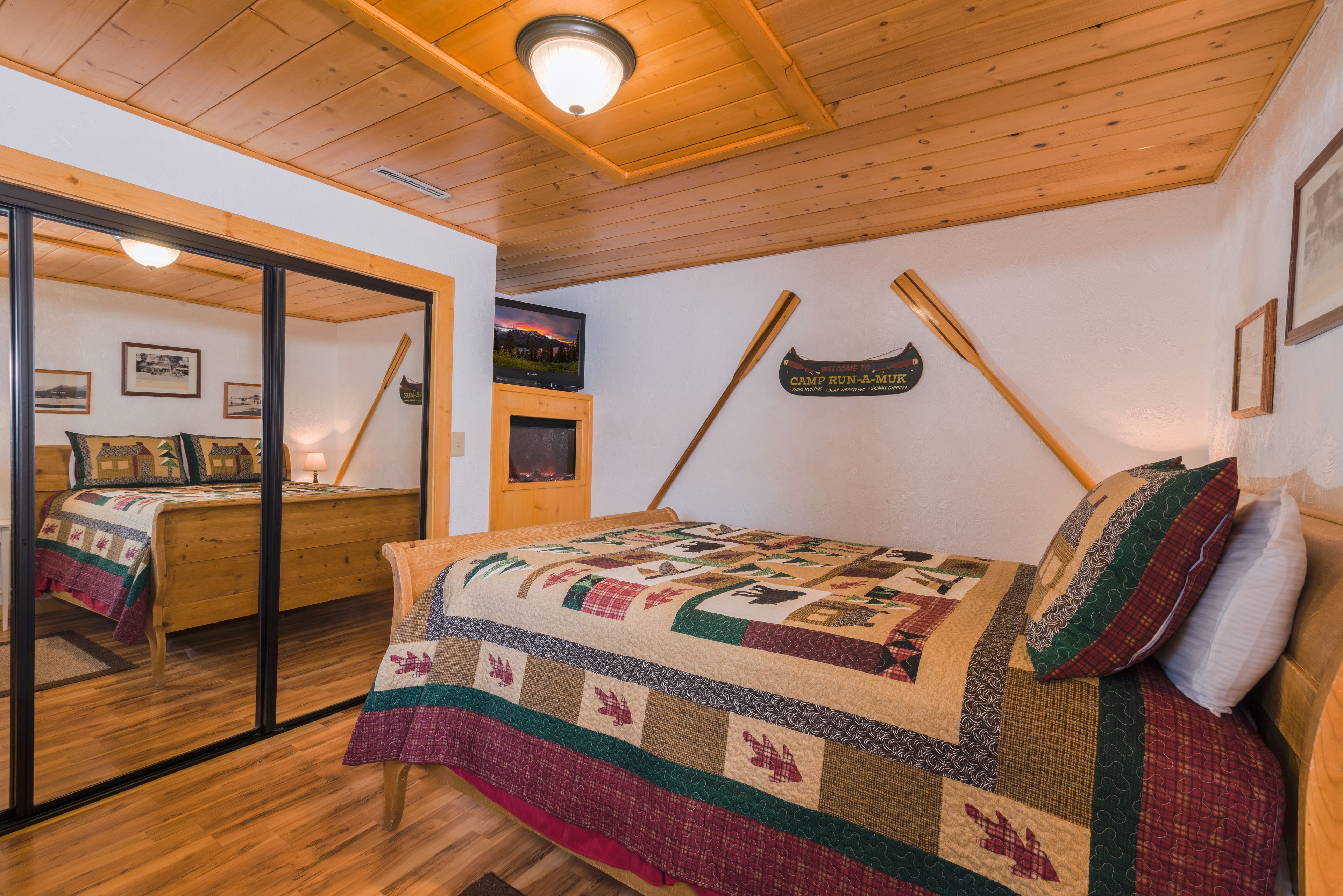 A cozy room with a wooden bed, a large mirror, and a quilt with a baseball theme.