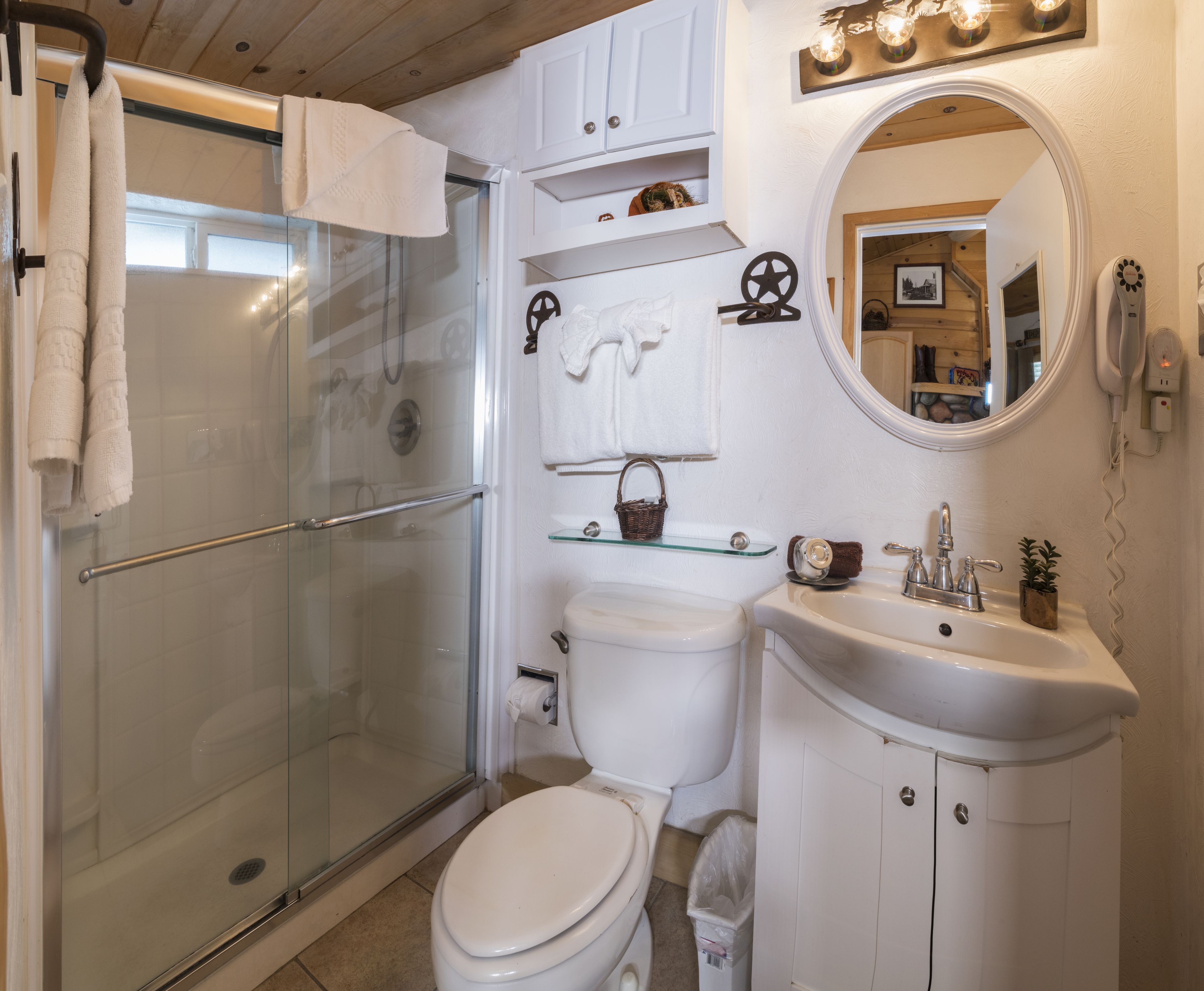 Une salle de bain avec une douche à parois de verre, des toilettes, un lavabo avec un miroir et un meuble-lavabo avec des placards.