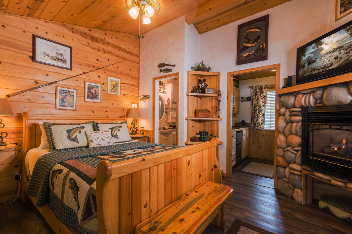 A cozy cabin-style room with a wooden bed, a stone fireplace, and a kitchen area.