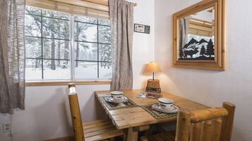 A wooden dining table with two plates and a lamp, set against a window with a view of snow-covered trees.