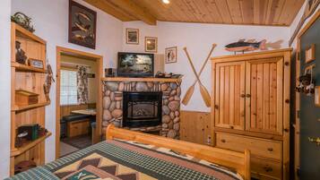 Ein gemütliches Zimmer mit Kamin aus Stein, Holzmöbeln und einem Bett mit gemustertem Überwurf.
