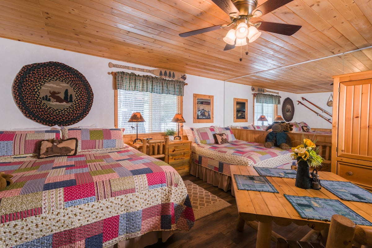 A cozy cabin-style room with two beds, a wooden ceiling fan, and a rustic decor.
