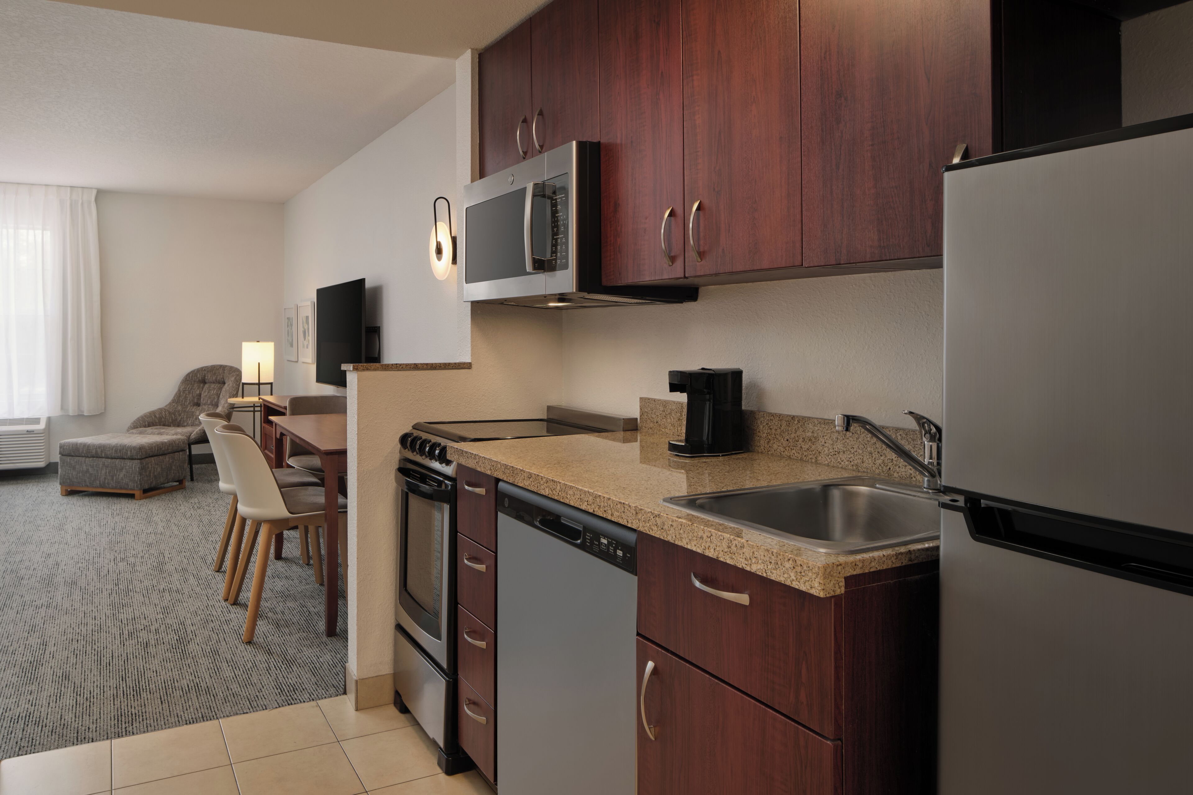 A modern kitchen with stainless steel appliances, wooden cabinets, a granite countertop, and a dining area with a sofa and table.