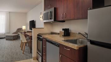 A modern kitchen with stainless steel appliances, wooden cabinets, a granite countertop, and a dining area with a sofa and table.