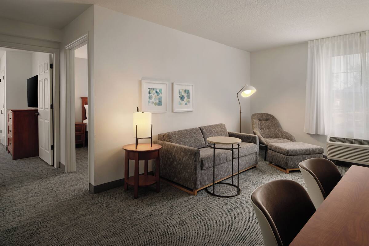 Une chambre d’hôtel avec un canapé, un fauteuil, une table ronde et un téléviseur dans un coin.