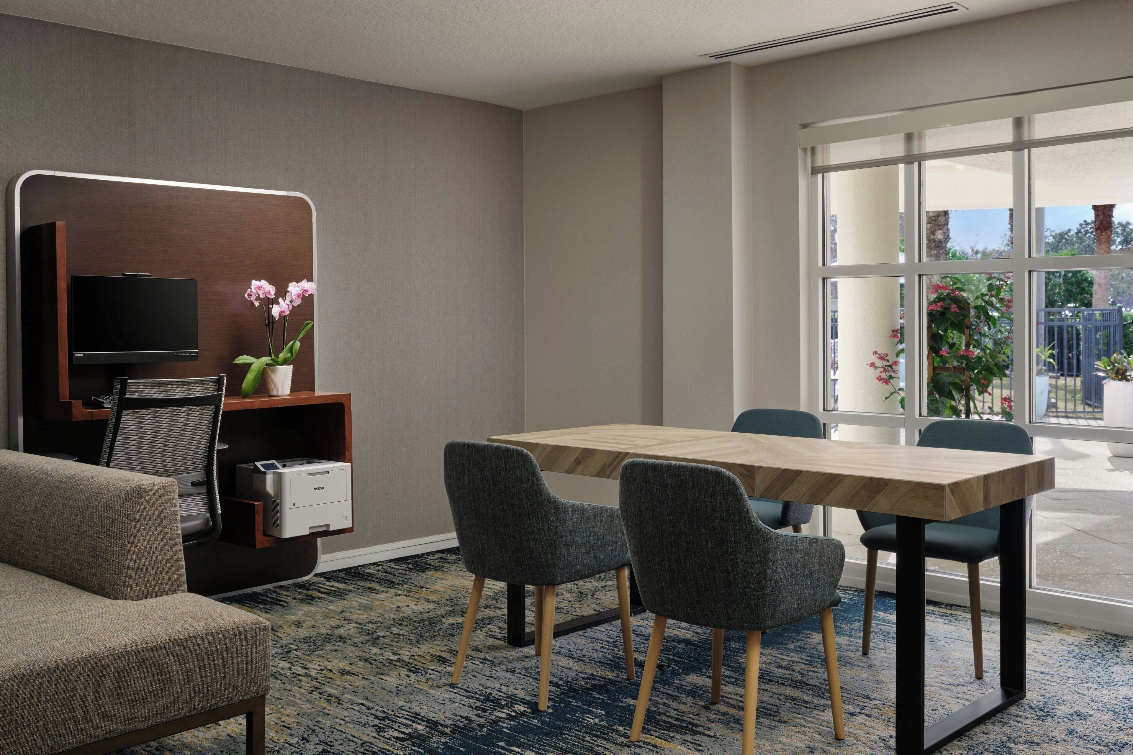 Habitación de hotel moderna con televisión de pantalla plana, un escritorio de madera, dos sillas, un sofá y un ventanal con vistas al exterior.