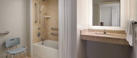 A bathroom with a shower, a bathtub, a handrail, a grab bar, a wheelchair, and a sink with a mirror.