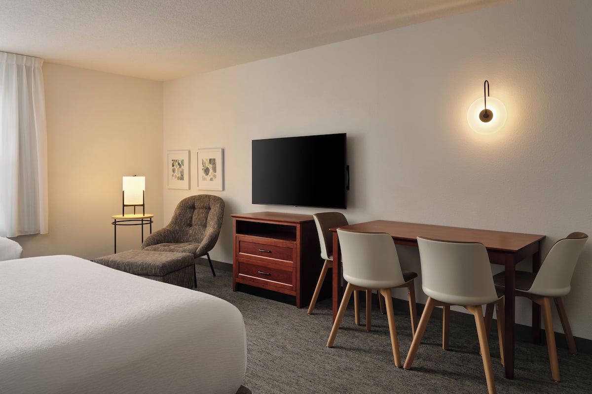 Une chambre d’hôtel avec un lit, un bureau avec des chaises, une télévision, une lampe et des œuvres d’art accrochées au mur.