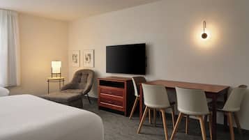 Una habitación de hotel con una cama, un escritorio con sillas, un televisor, una lámpara y obras de arte en la pared.