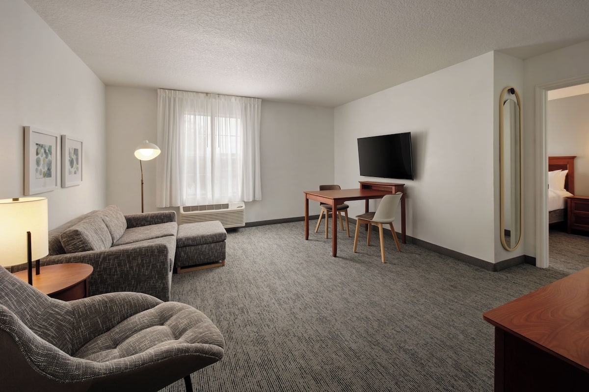 Une chambre d’hôtel avec un canapé, une petite table, une télévision et un miroir.