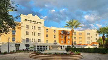 A hotel with a fountain in the courtyard, surrounded by palm trees and a paved walkway.