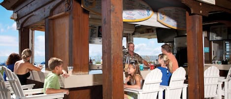 A wooden outdoor seating area with white Adirondack chairs and a wooden structure overhead.
