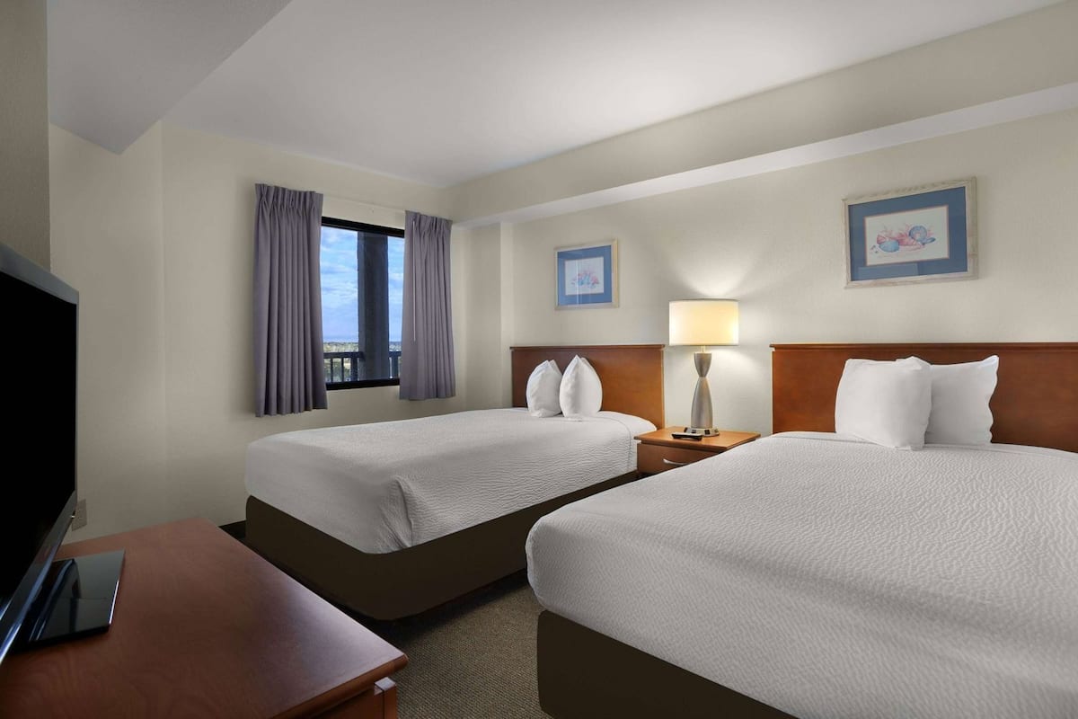 Quarto de hotel com duas camas, televisão, secretária e janela com cortinas.